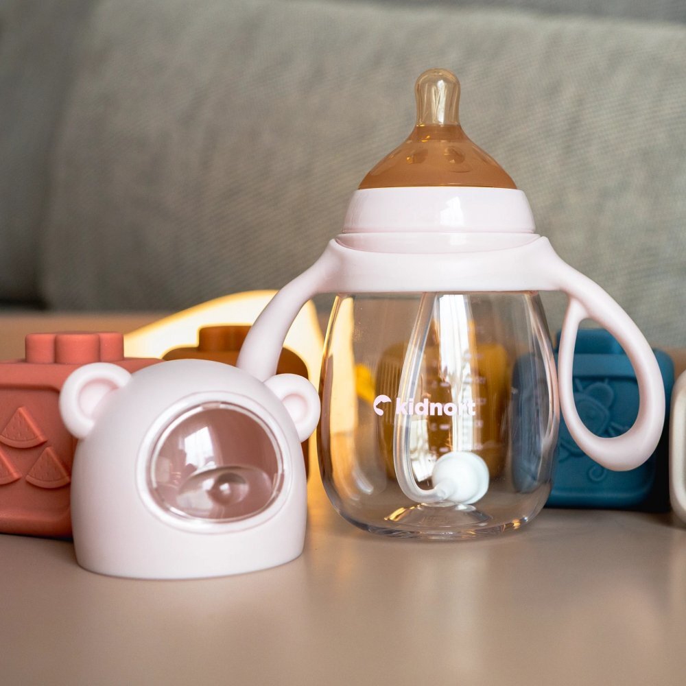 Kidnort Biberon cu tetina anti-colici debit variabil Jordbaer Pink 240ml de la 6 luni echipat cu Pai cu bila gravitationala si maner ergonomic detasabil